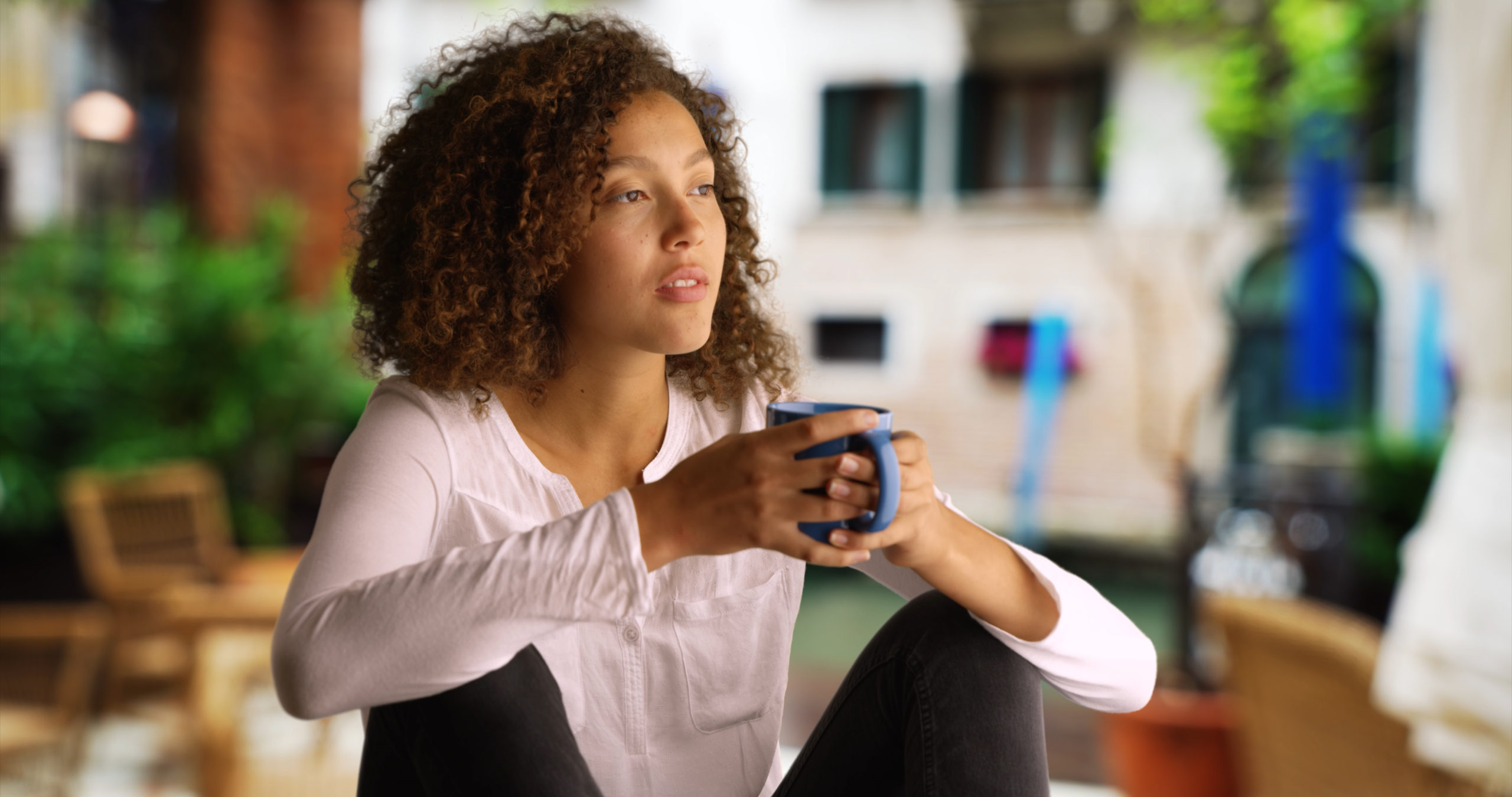 Pretty black woman with curly hair sits outside drinking coffee