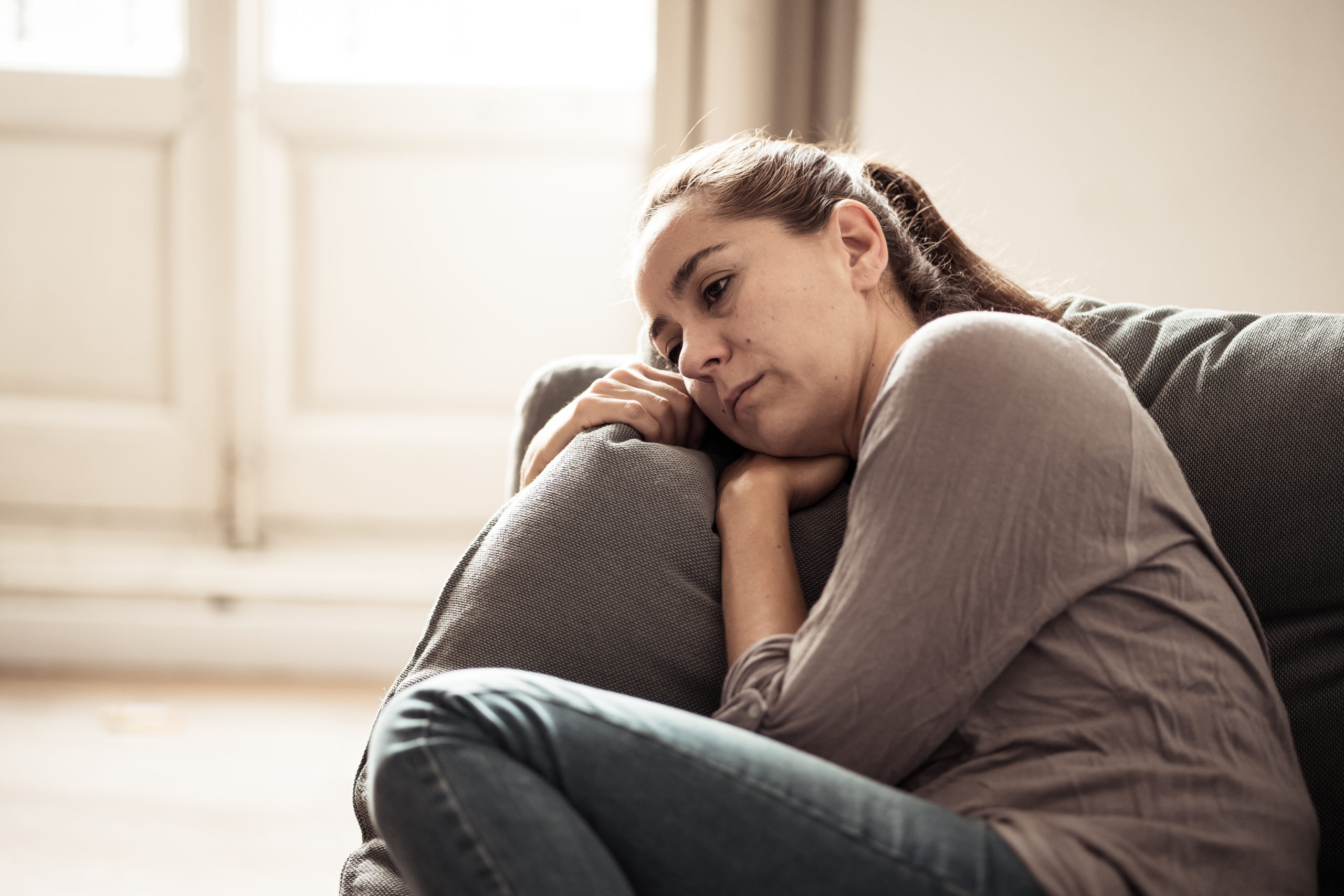 Young woman suffering from depression feeling sad and lonely on sofa at home